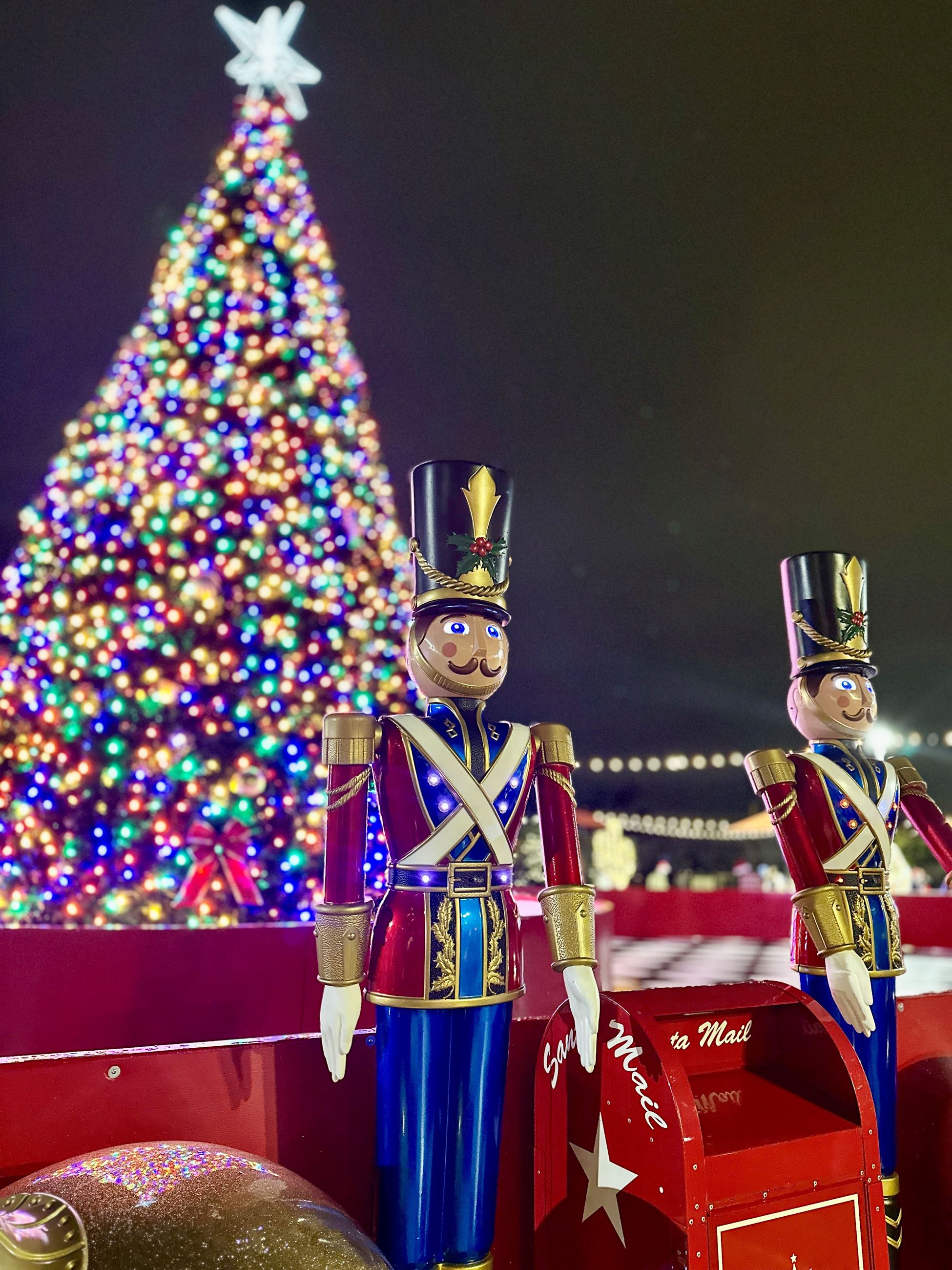 Picture of two nutcracker statues standing in front of a large bright Christmas Tree
